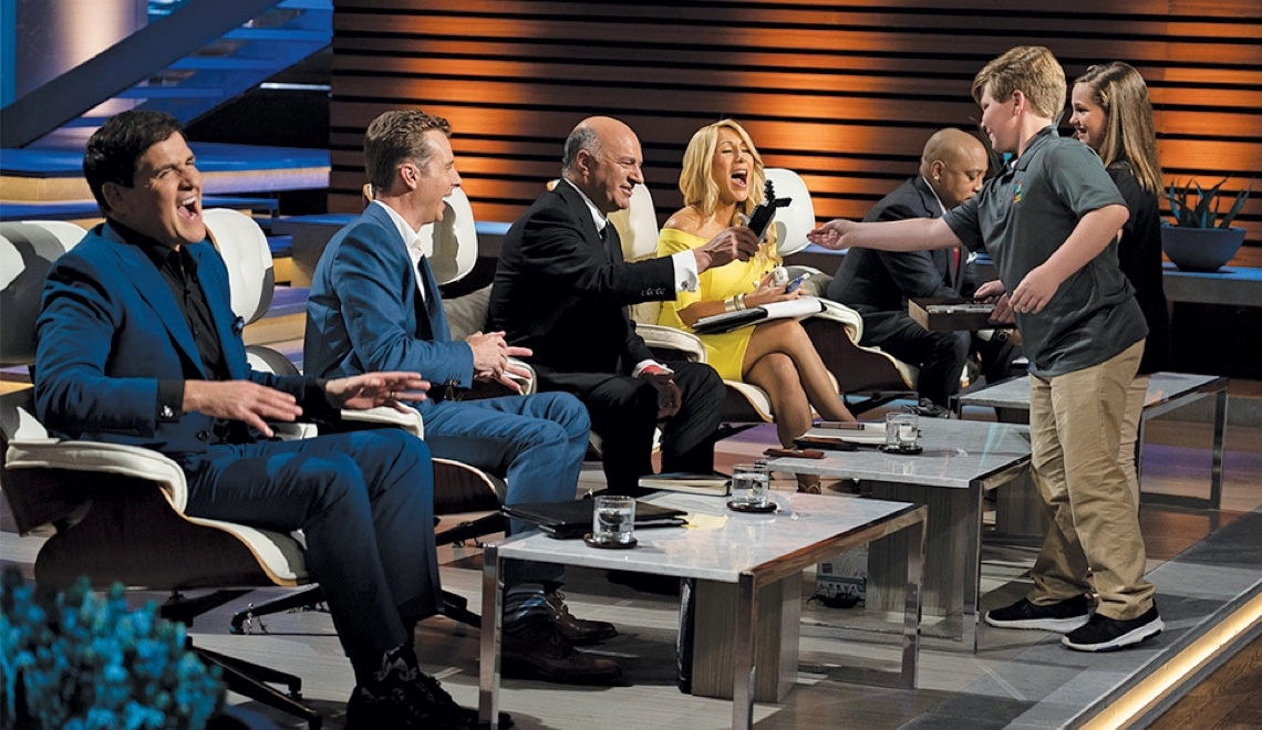 child showing shark tank panel a product on set